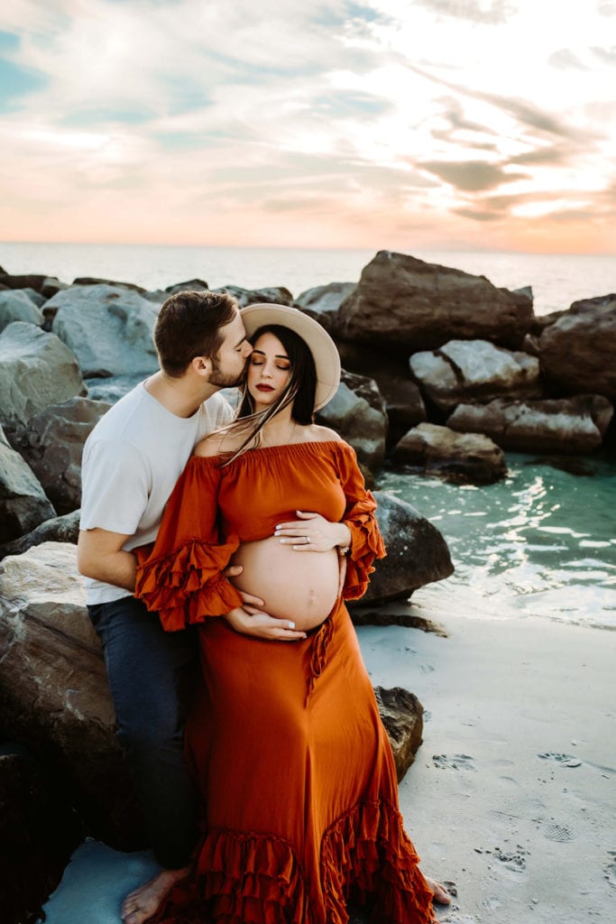 Maternity Photographer, husband and expectant wife embrace near the ocean