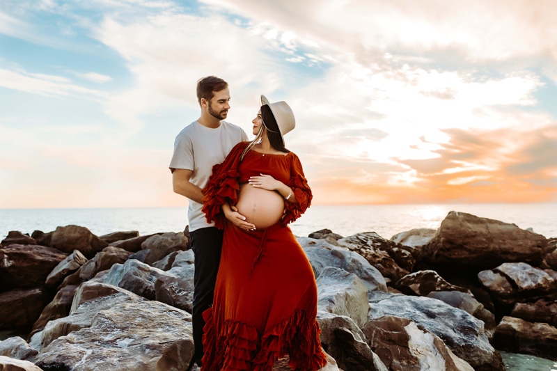 Maternity Photograph, man and expecting partner embrace on rocks near the ocean